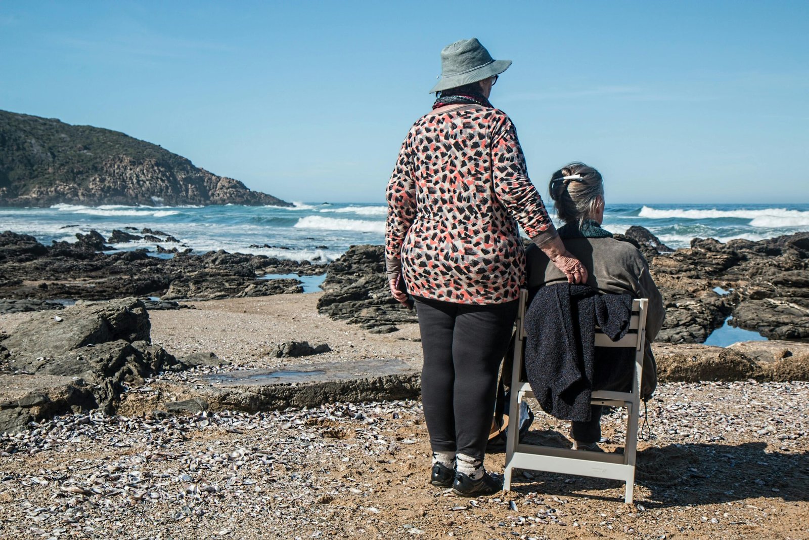 women-friends-friendship-helping-together-160767-160767 Two senior women enjoying a peaceful moment by the rocky beach, embracing friendship and serenity.